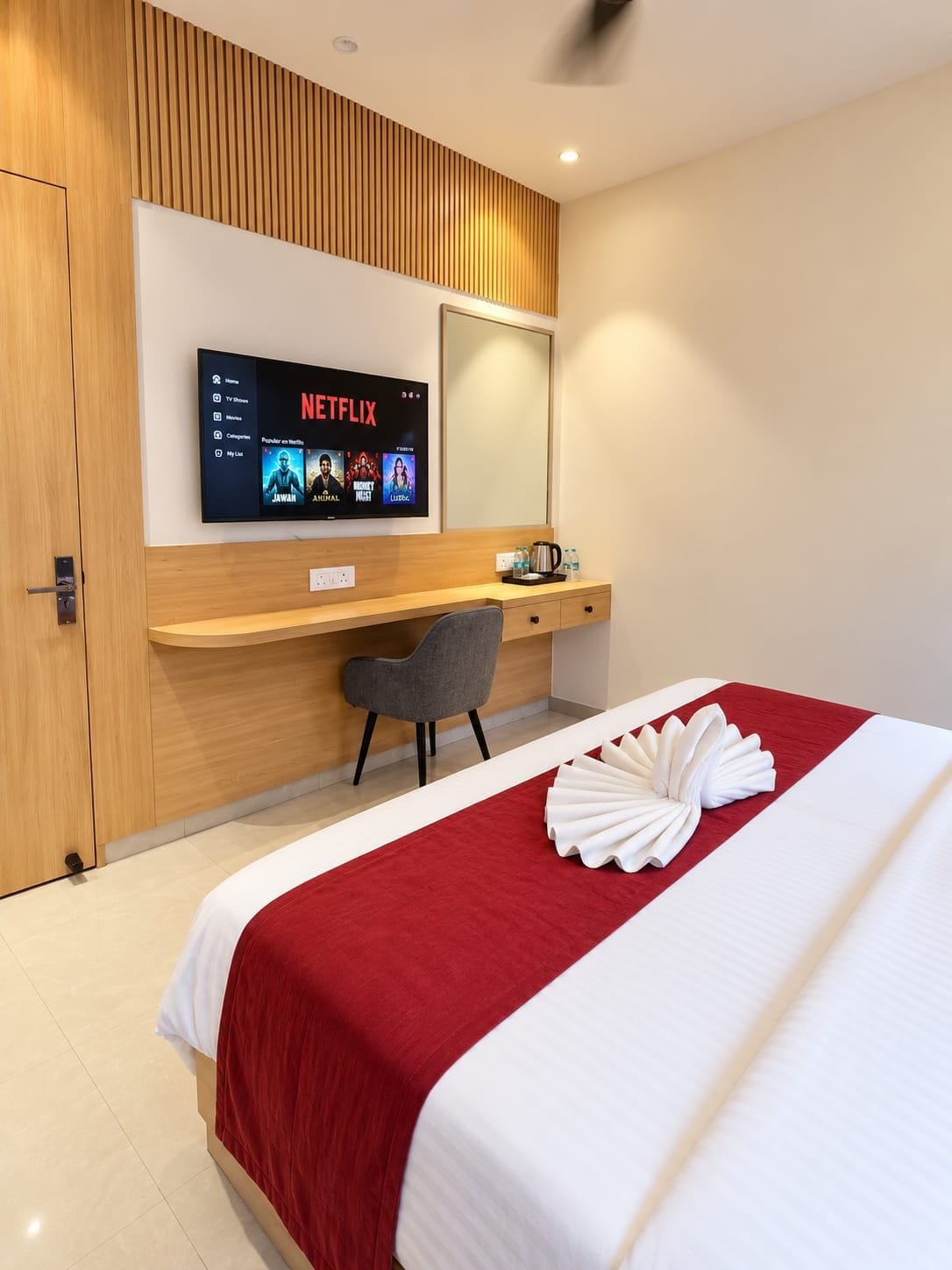 A hotel room with a bed, a desk, a chair, a TV mounted on the wall, and a wooden panel design.