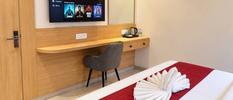 A hotel room with a bed, a desk, a chair, a TV mounted on the wall, and a wooden panel design.