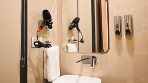 Un baño con un lavamanos blanco, un espejo, una toalla y un secador de pelo en un soporte de pared.