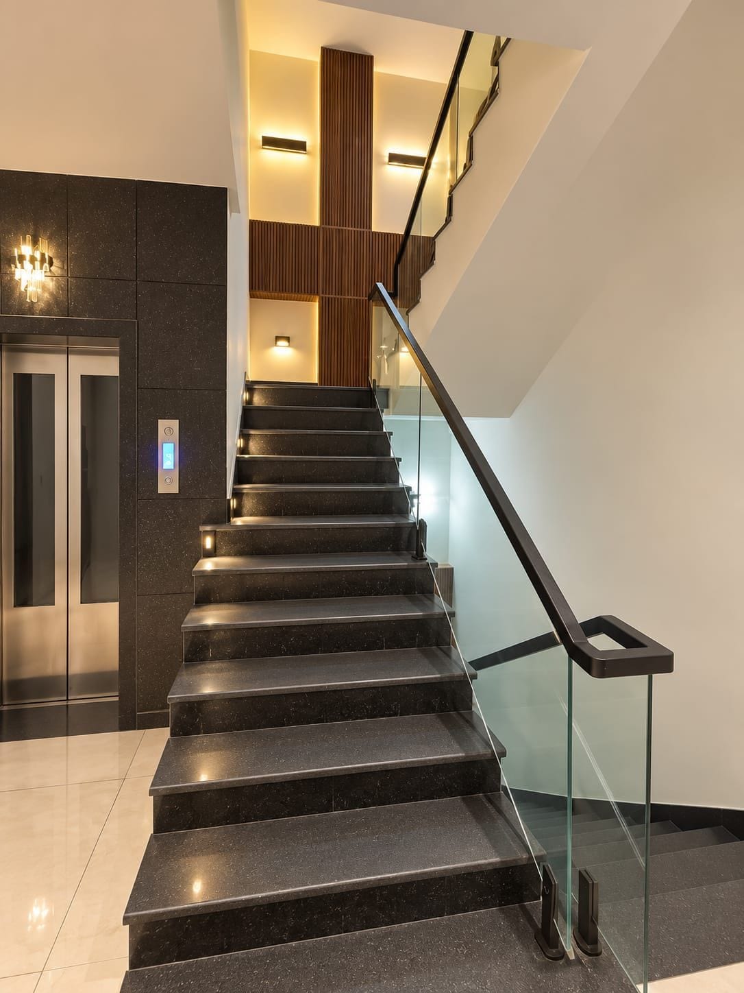 A modern staircase with glass railings, a built-in elevator, and ambient lighting.