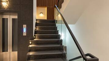 A modern staircase with glass railings, a built-in elevator, and ambient lighting.
