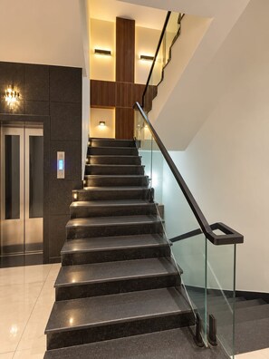 A modern staircase with glass railings, a built-in elevator, and ambient lighting. - Hotel Vyom Residency (sunderpur)