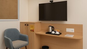 Une chambre d’hôtel équipée d’un bureau en bois, d’une chaise, d’une télévision, d’une machine à café et d’une poubelle.
