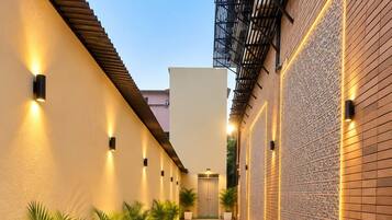 A corridor with a patterned floor, walls with decorative lighting, and potted plants lining the path.