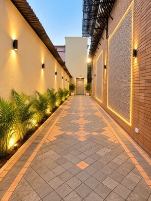 Un couloir doté d’un sol à motifs, de murs éclairés par des luminaires décoratifs et de plantes en pot disposées le long du chemin.