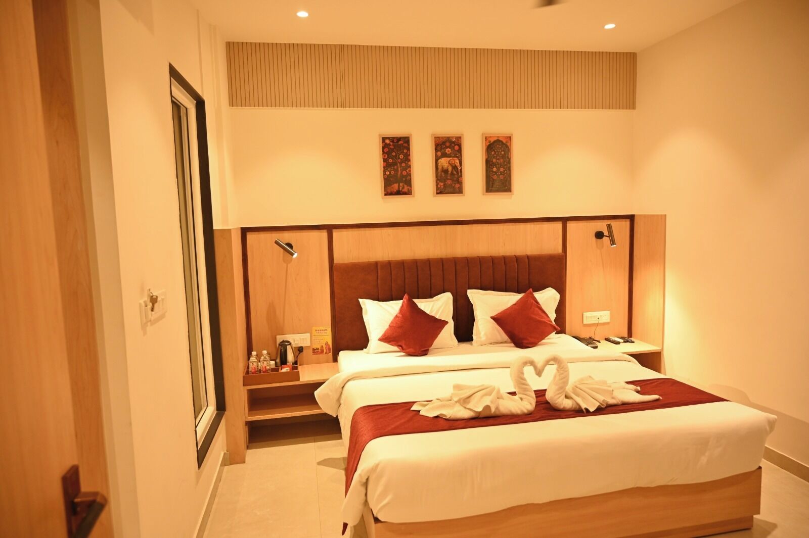 A hotel room with a large bed, two bedside tables, a wooden headboard, and three wall-mounted artworks.