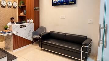 Un área de recepción con mostrador, un sofá de cuero negro, un televisor de pared mostrando contenido de Netflix y un reloj con indicaciones para Nueva York, Londres y Tokio.