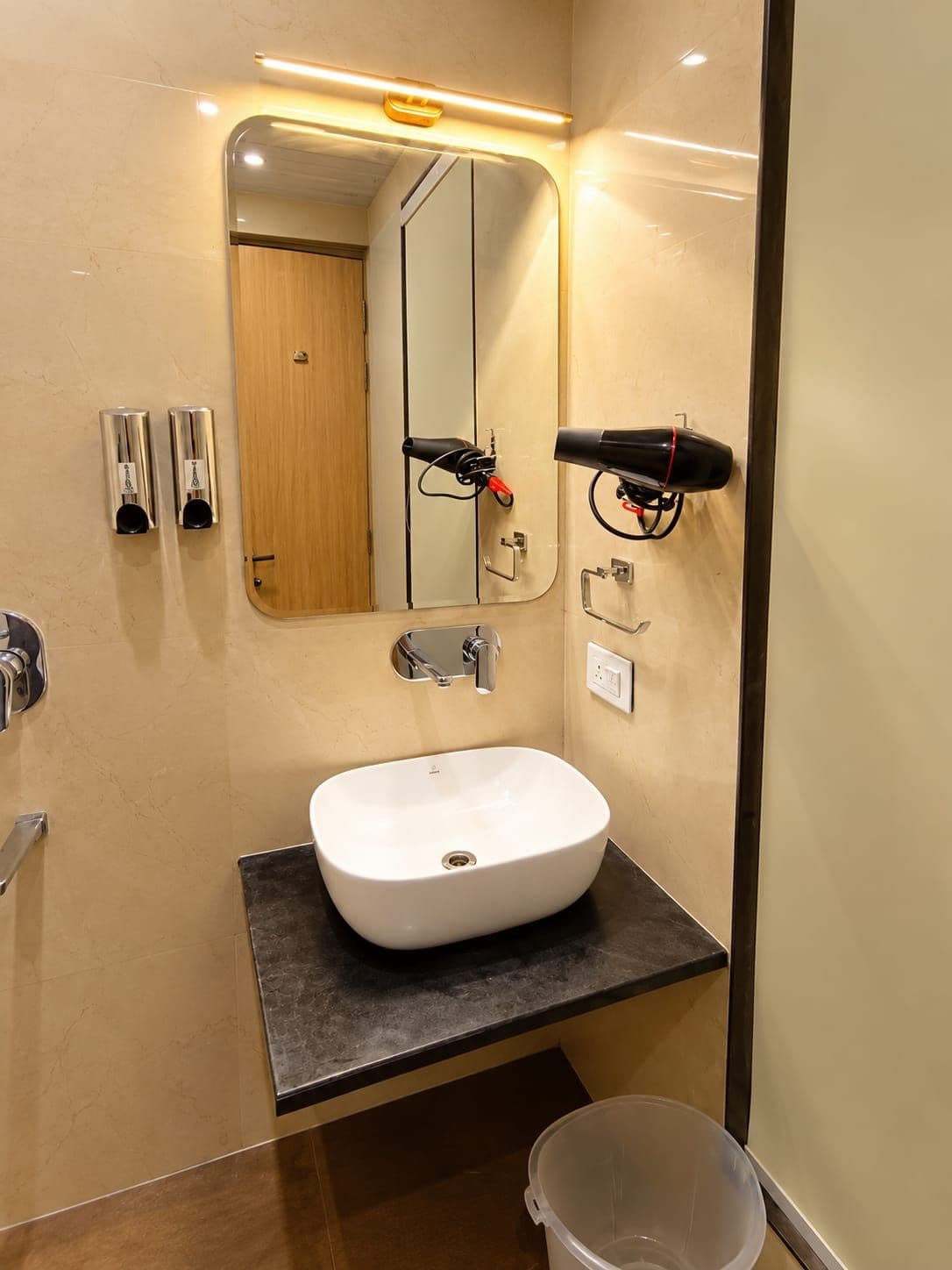 A bathroom with a white sink, a mirror, a hairdryer, and a trash bin.