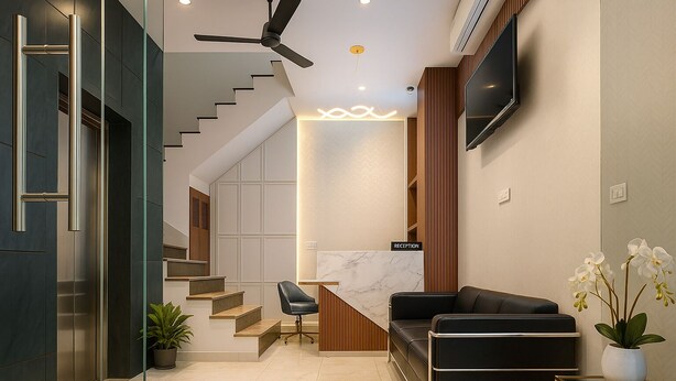 Un intérieur moderne comprenant un comptoir d’accueil, un escalier, un canapé en cuir noir et un téléviseur à écran plat fixé au mur.