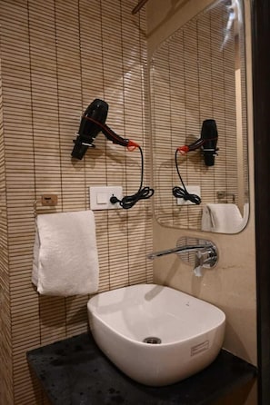 Un baño con lavamanos blanco, toallero, espejo y secador de pelo montado en la pared.