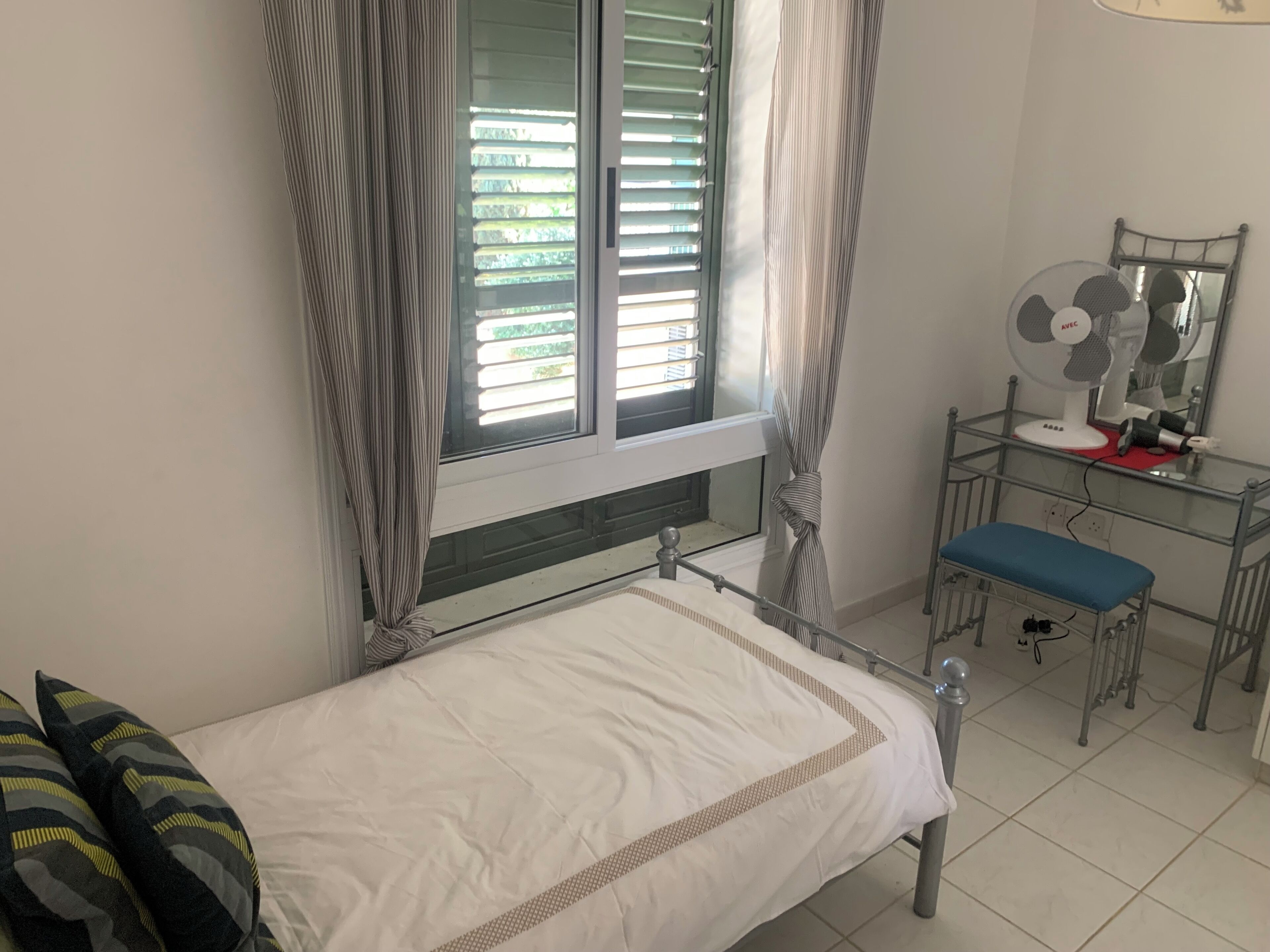 Un dormitorio con cama, un escritorio con espejo y una ventana con persianas.