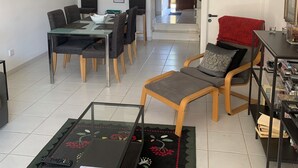 Ein modernes Wohnzimmer mit Essbereich, einer Küche im Hintergrund und einer roten Tür zu einem weiteren Raum.