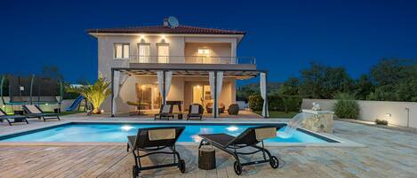 A two-story house with a swimming pool, outdoor seating, and a covered patio.