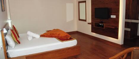 Un dormitorio con cama de madera, televisor montado en la pared y una silla de madera.