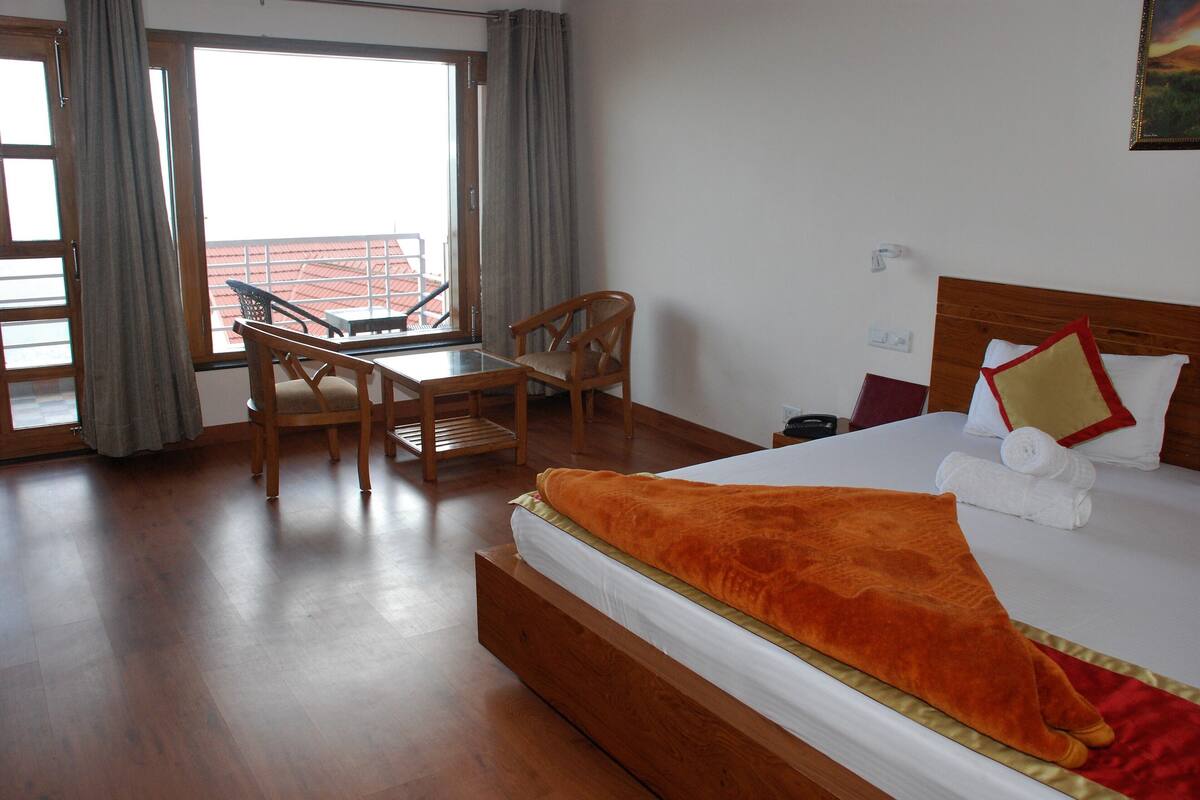 Une chambre d’hôtel avec un lit, un bureau, deux chaises et une vue sur un balcon.
