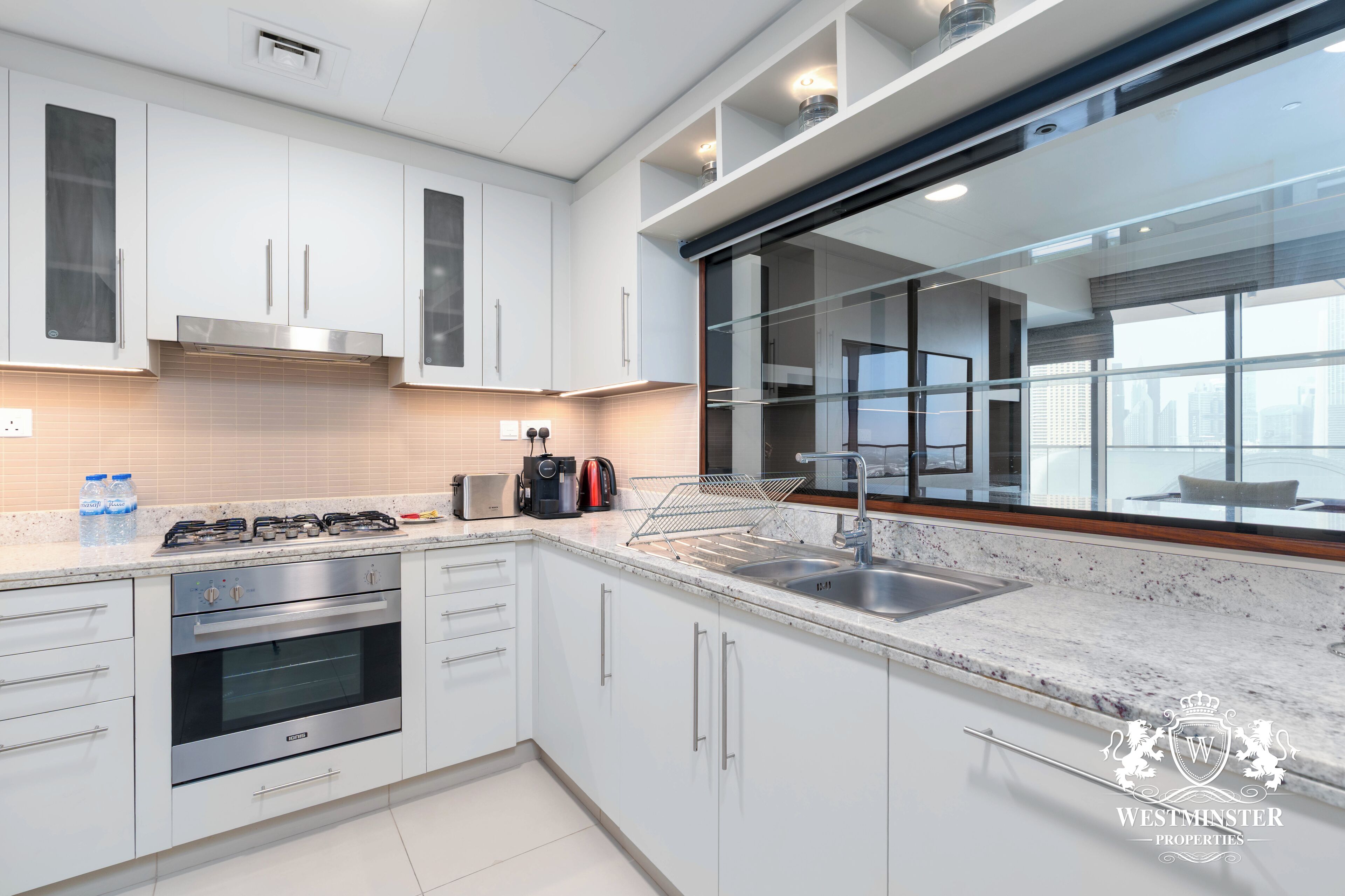 A modern kitchen with white cabinetry, a stainless steel range, and a large window offering a city view.