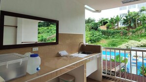 A bathroom with a sink, mirror, and a view of a pool and greenery. - DMC Condotel (Puerto Princesa)