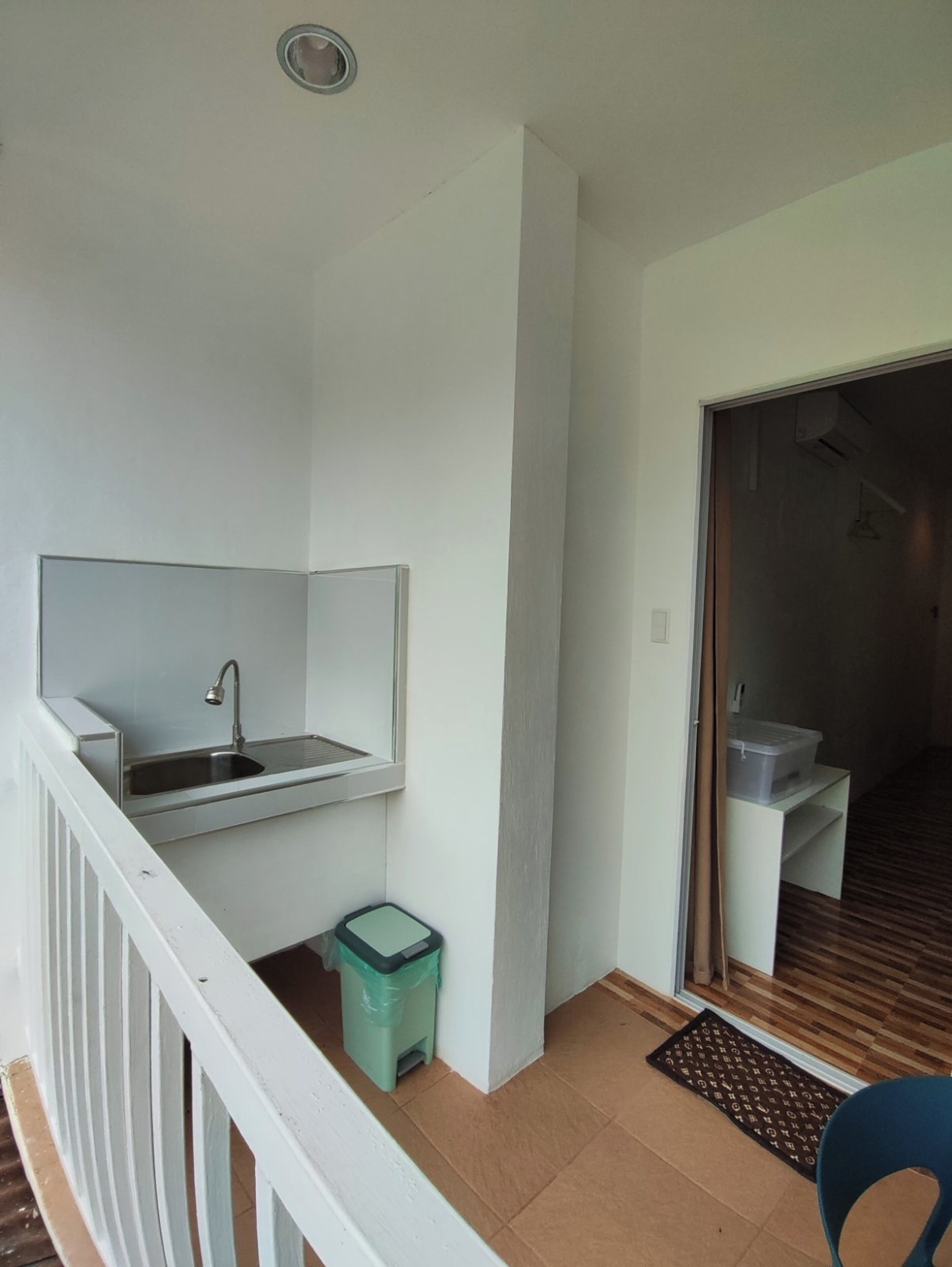 A small balcony with a sink, a trash bin, and a door leading to a dark interior.