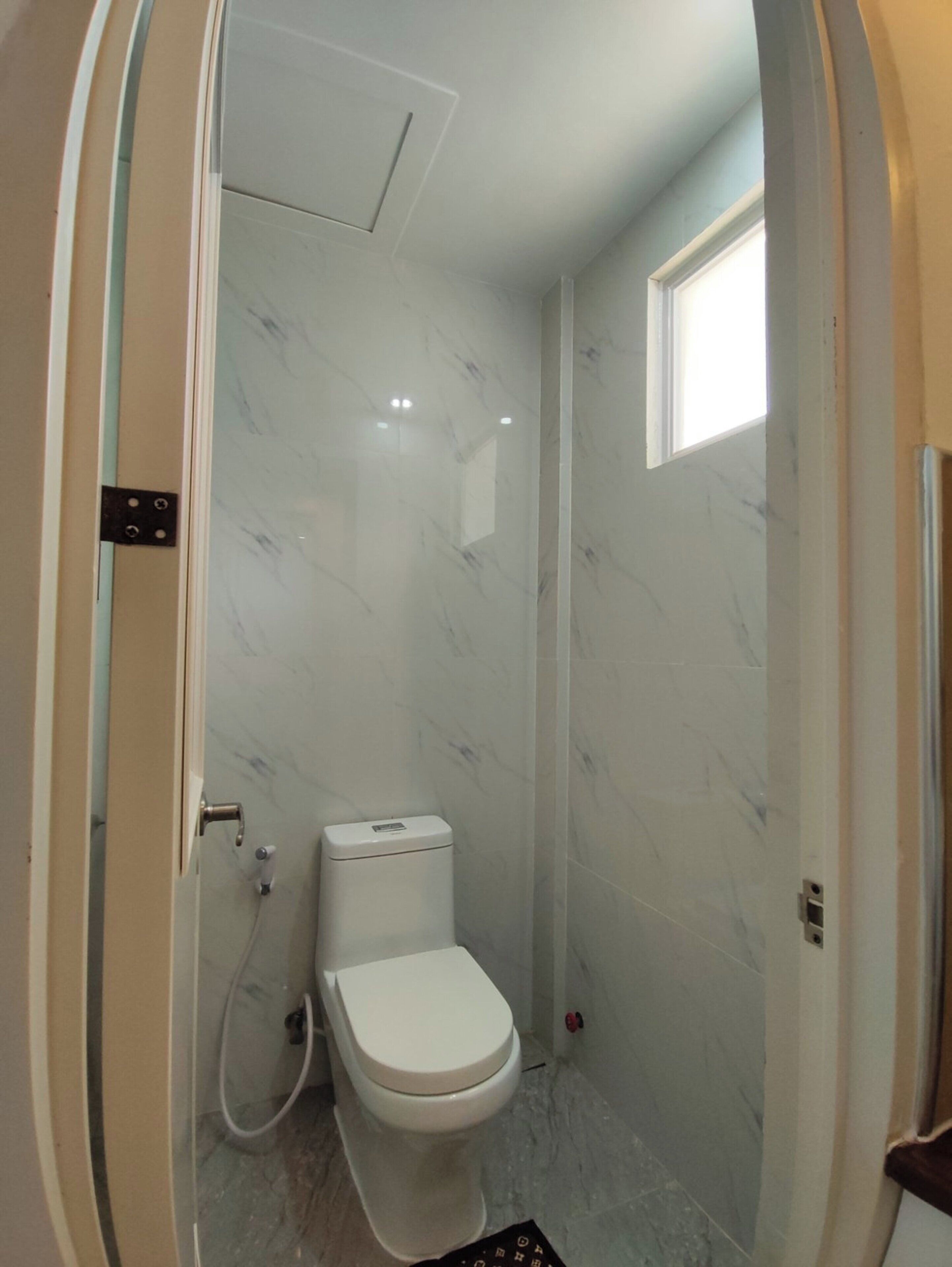 A small bathroom with a toilet, a shower, and a window.