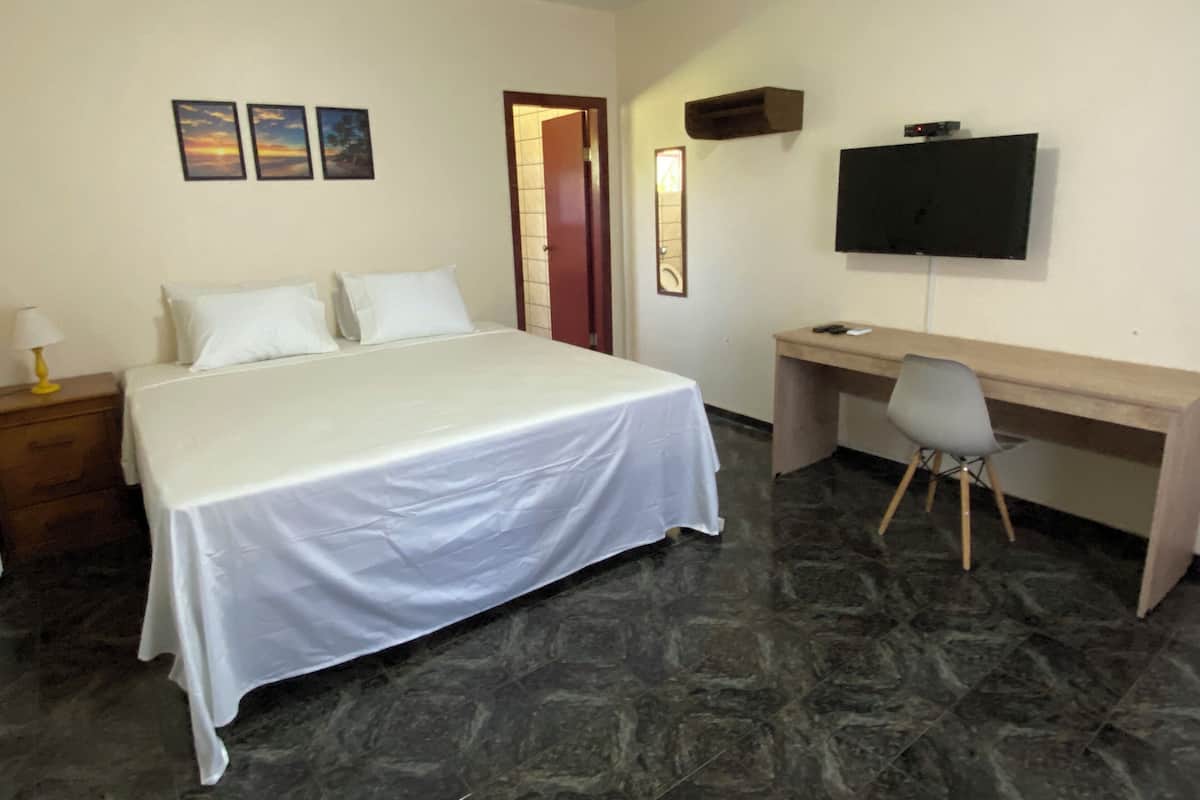 Una habitación de hotel con una cama, un escritorio, una silla, un televisor y una puerta.