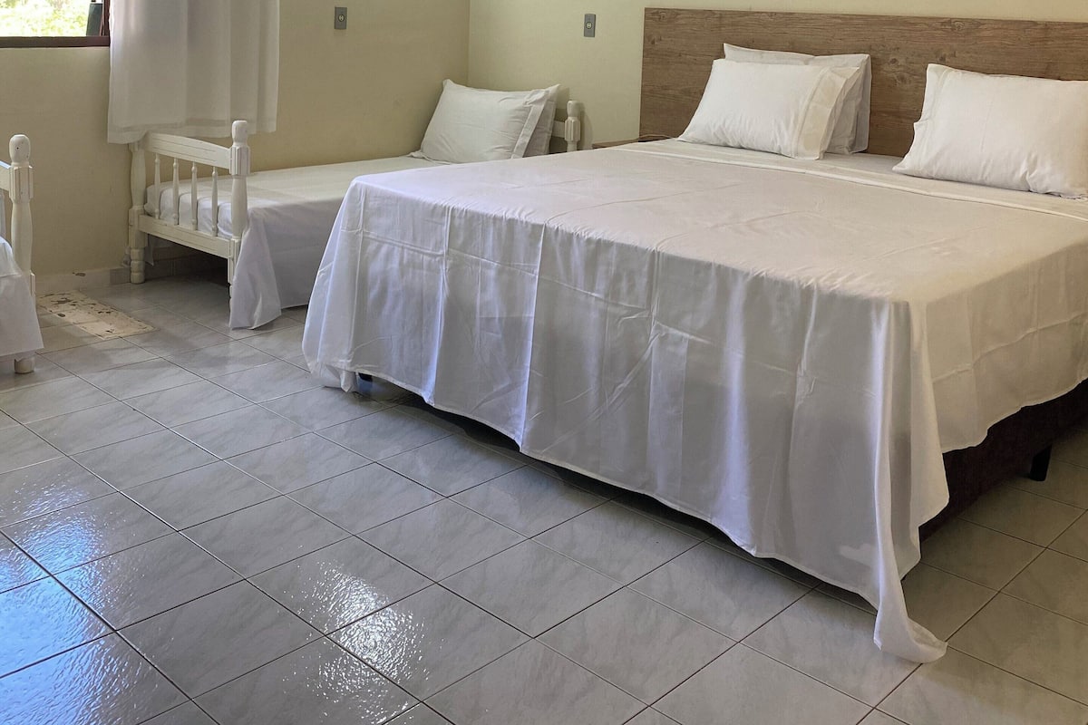 Una habitación de hotel con una cama grande, una mesita de noche pequeña, una ventana con cortinas y un aire acondicionado instalado en la pared.