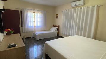 Habitación de hotel con dos camas, un escritorio, una silla, un ventanal con cortinas y un equipo de aire acondicionado.