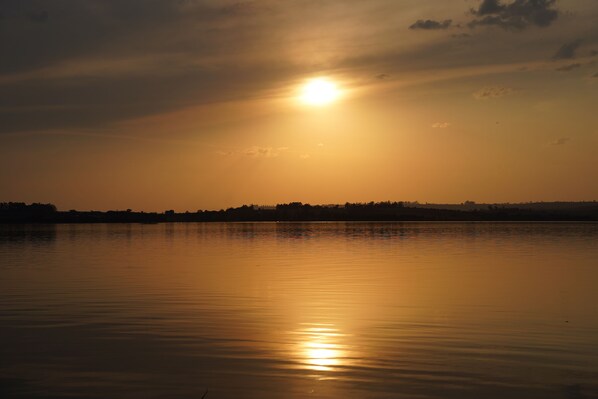 A sunset over a calm body of water with a silhouette of trees in the background.