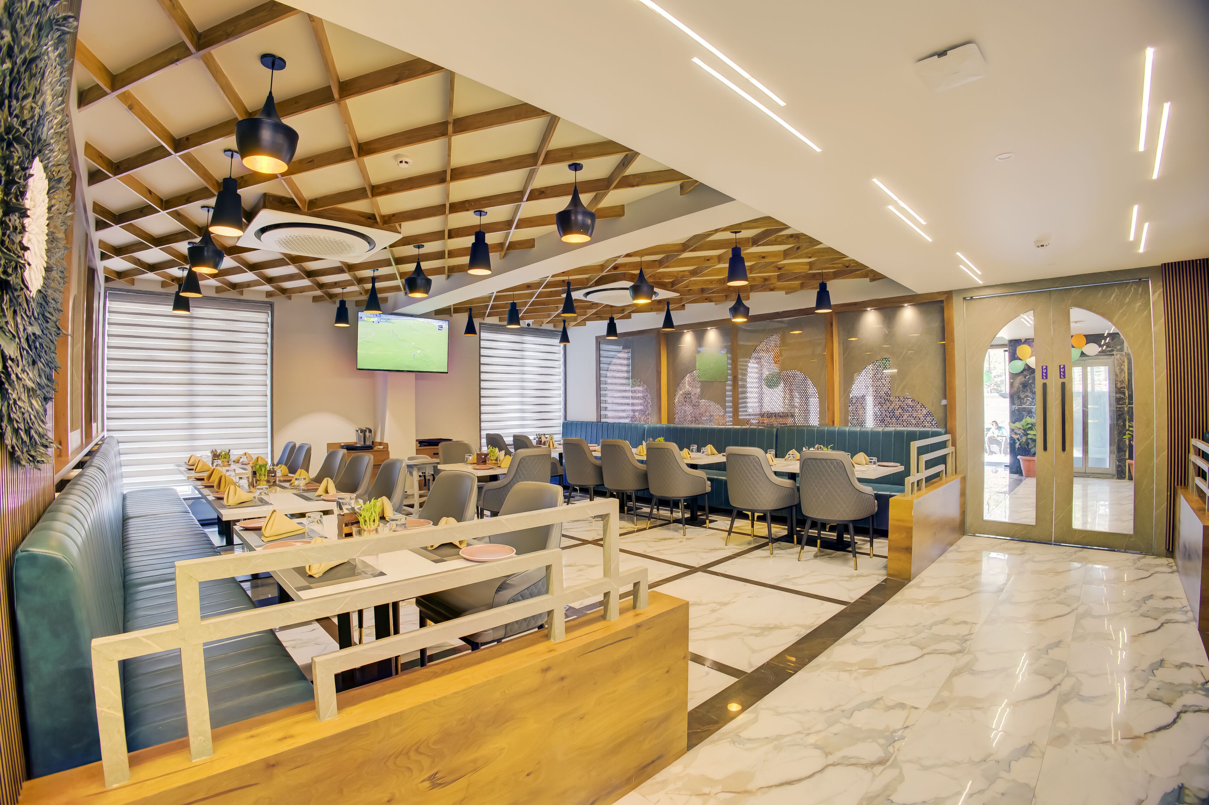 A modern restaurant with a long communal dining table, individual booths, and a wooden ceiling.
