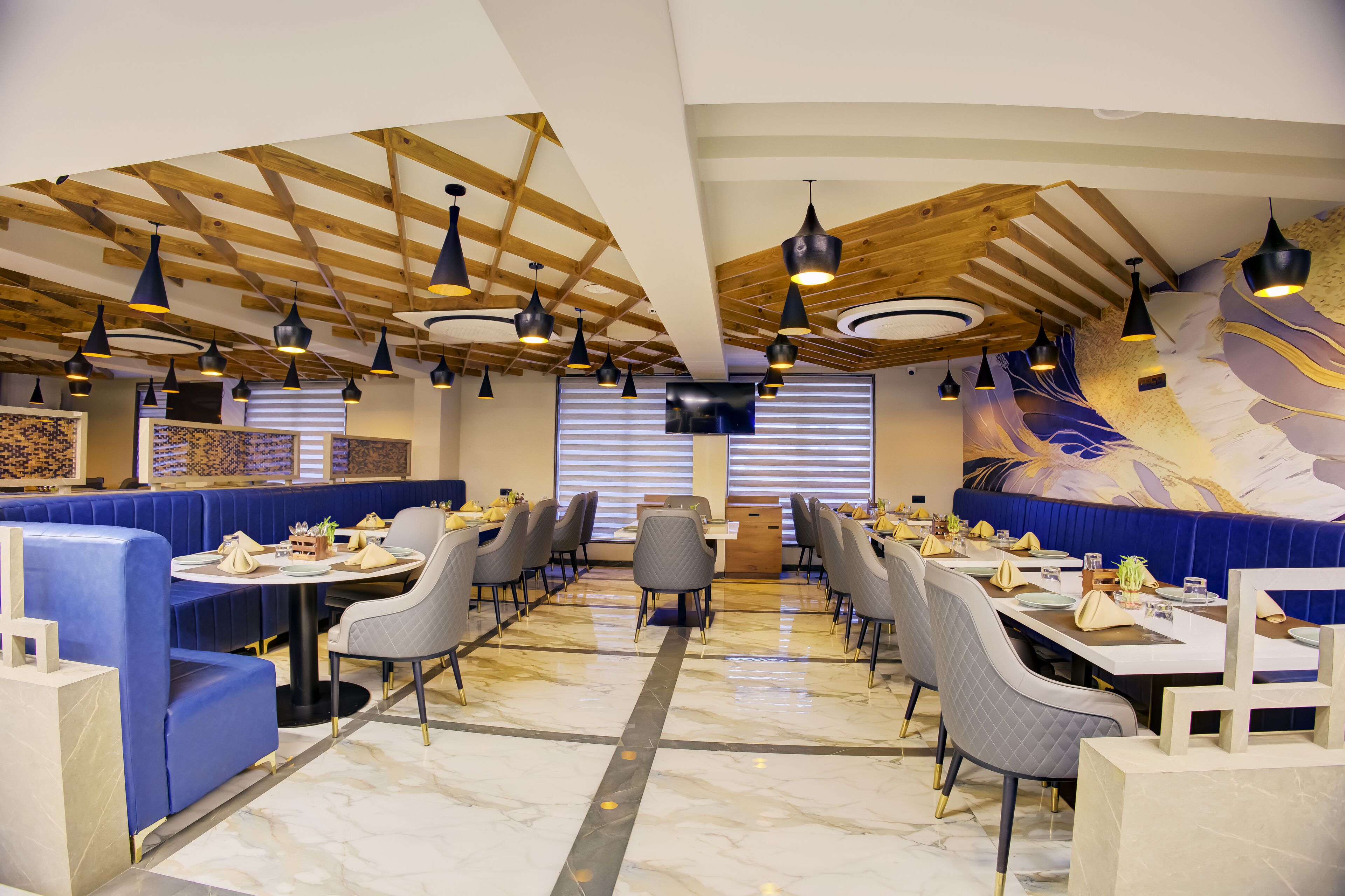 A restaurant with booths and tables, wooden ceiling beams, and pendant lighting.