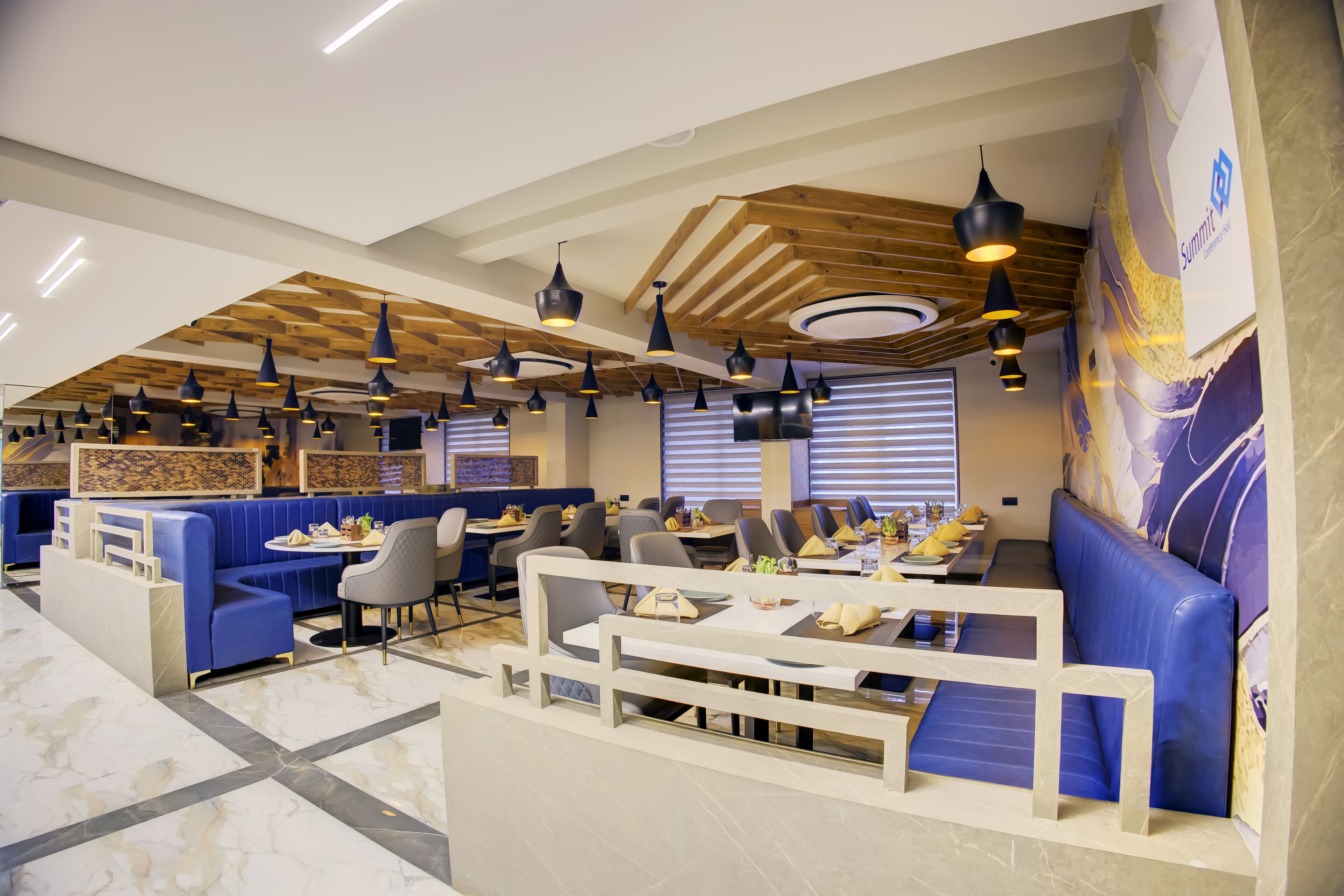 Un restaurante moderno con asientos tipo banqueta azules, vigas de madera en el techo e iluminación colgante.