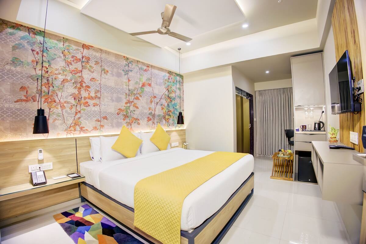 Quarto de hotel moderno com uma cama grande, uma escrivaninha, televisão e um banheiro visível por uma porta aberta.