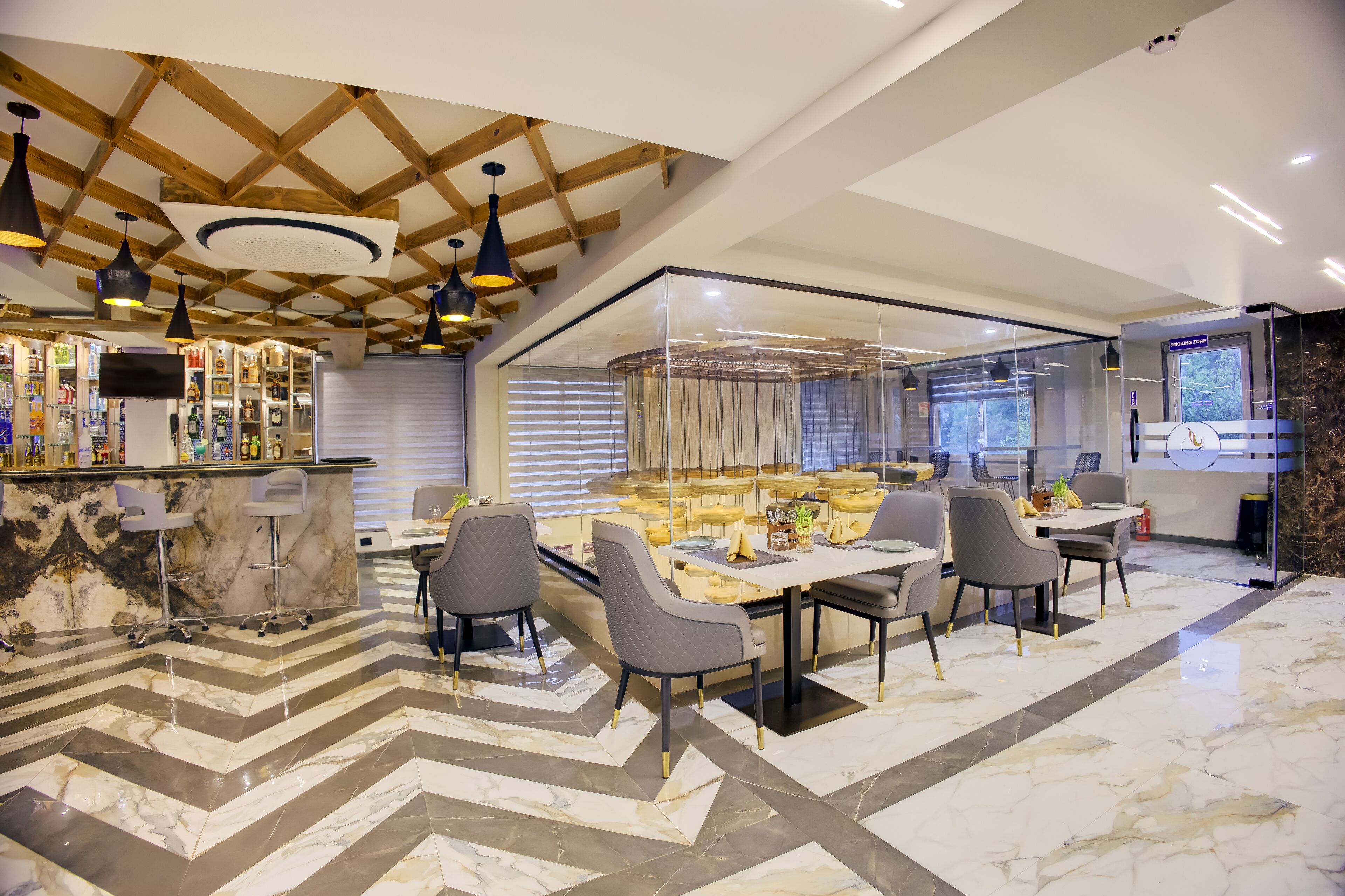 Un moderno hall de hotel con zona de bar, asientos separados por un panel de vidrio y suelo de mármol.