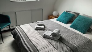 A bedroom with a skylight, a bed with patterned bedding, a teal chair, and a bedside table with a lamp. - 4-bedroom house for 8 people, 7 km from the beach. (Plouégat-Guérand)