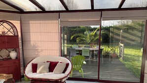 A room with a wicker chair, a small table, and a glass door leading to an outdoor patio with a table and chairs. - 4-bedroom house for 8 people, 7 km from the beach. (Plouégat-Guérand)
