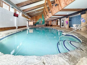 An indoor swimming pool with wooden beams, a tiled floor, and a safety sign on the wall.