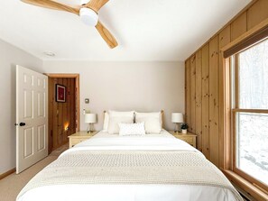 A bedroom with a bed, two bedside tables, a ceiling fan, a window, and wooden walls. - Chimney Hill Haven | Close to Mt.Snow (Wilmington)