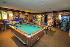 A pool table with a green felt surface, surrounded by arcade machines and a dartboard.