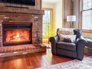 Una sala de estar con chimenea, un sofá de cuero y un ventanal con vistas a árboles.