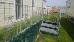 A mobile home with a metal fence and a small set of stairs leading to the entrance. - Spacious 6 berth caravan with decking. Indoor Heated pool on site!! (Burnham-on-Sea)