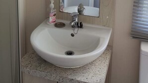 A bathroom with a white sink, a mirror, and a wooden cabinet. - Spacious 6 berth caravan with decking. Indoor Heated pool on site!! (Burnham-on-Sea)
