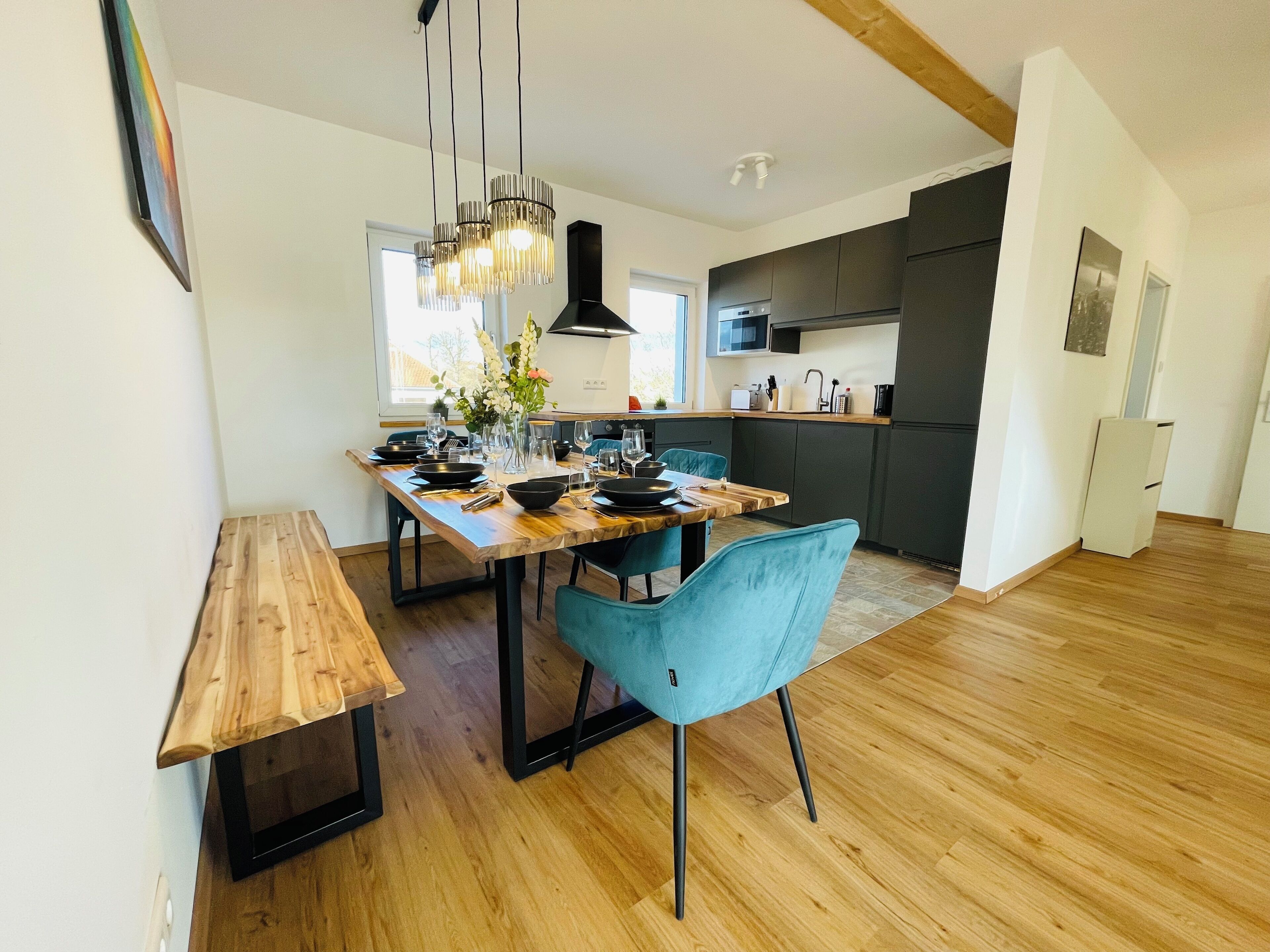 A modern kitchen with dark cabinets, a wooden dining table, and blue chairs.