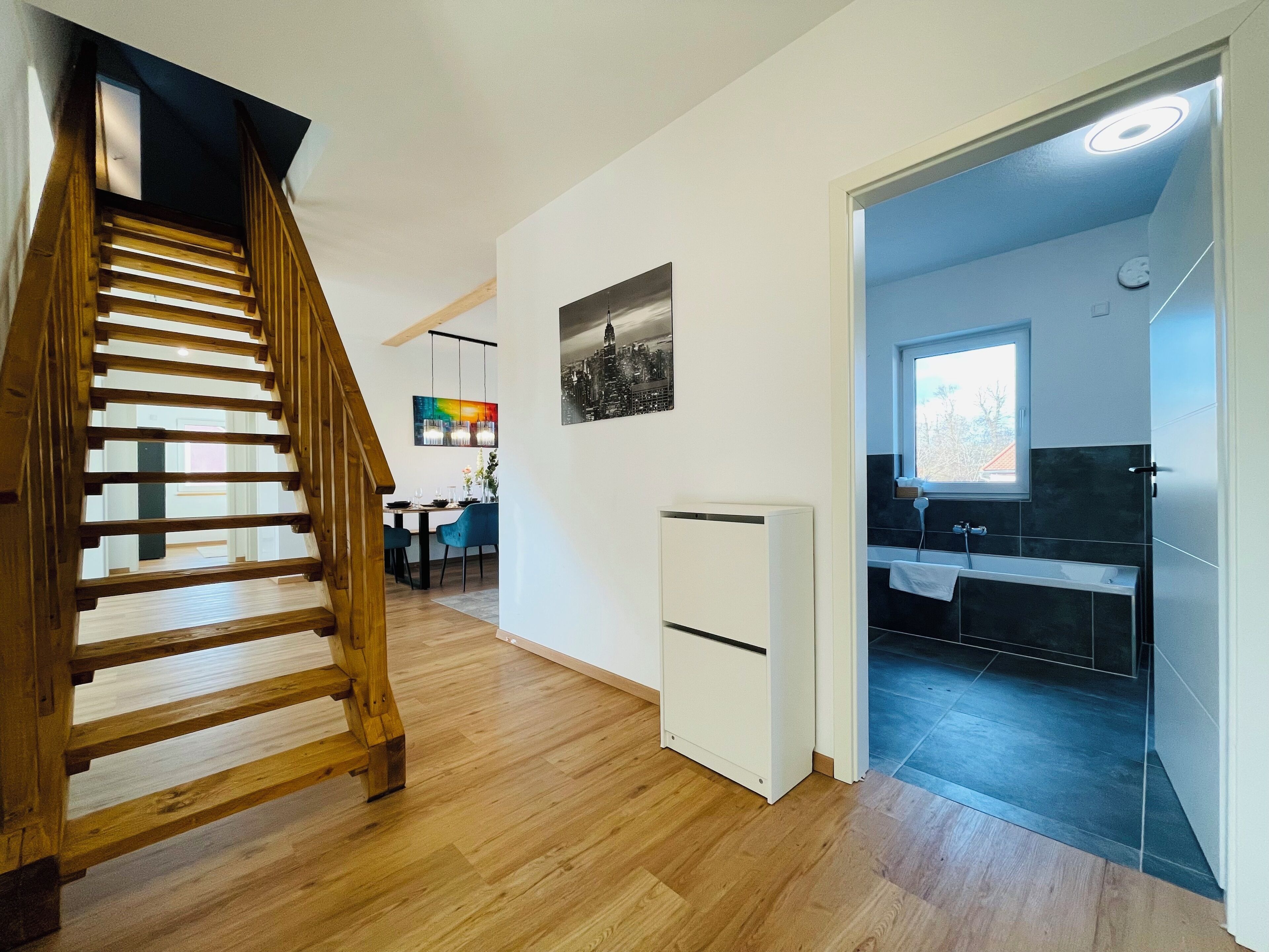 Un interior moderno con una escalera de madera, un comedor y un baño con ventana.