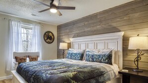 Une chambre avec un grand lit, des murs recouverts de panneaux en bois, un ventilateur de plafond et deux lampes de chevet.
