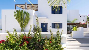 Edifici blanc amb porta i finestres blaves, envoltat de vegetació i cactus.
