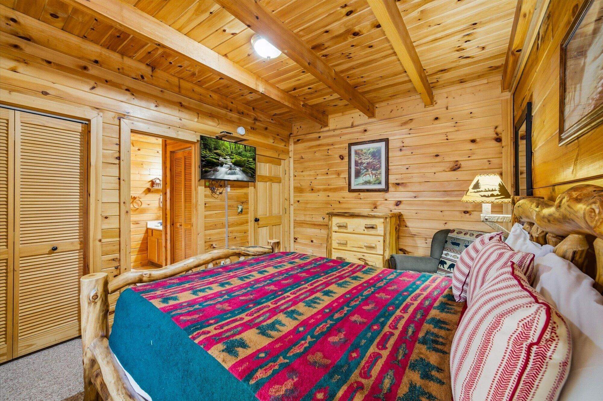 Une chambre de style rustique, avec un lit, une télévision, une commode et un tableau encadré au mur.