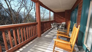 A wooden deck with a railing, a table with chairs, and a window with blinds. - Dream Chaser: Minutes from Dollywood & Downtown (Pigeon Forge)