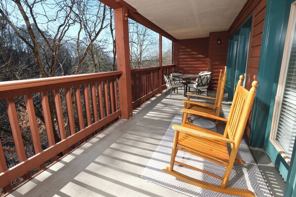 A wooden deck with a railing, a table with chairs, and a window with blinds. - Dream Chaser: Minutes from Dollywood & Downtown (Pigeon Forge)