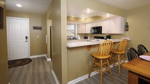 A compact kitchen with white cabinets, a black microwave, and a wooden dining table with four chairs. - Dream Chaser: Minutes from Dollywood & Downtown (Pigeon Forge)