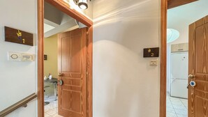 A hallway with wooden doors marked 1 and 2, a light fixture, and a kitchen area in the background. - Alisahni Home 1 (Chania)