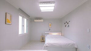 Un dormitorio con dos camas, una ventana, aire acondicionado y una mesita de noche con un florero.